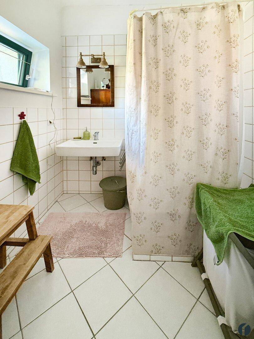 Badezimmer mit weißen Fliesen, Duschvorhang und kleinem Fenster.