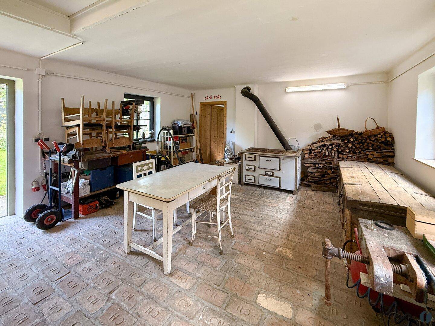 Geräumiger Hauswirtschaftsraum mit Ziegelboden, Werkbank und traditionellem Ofen.