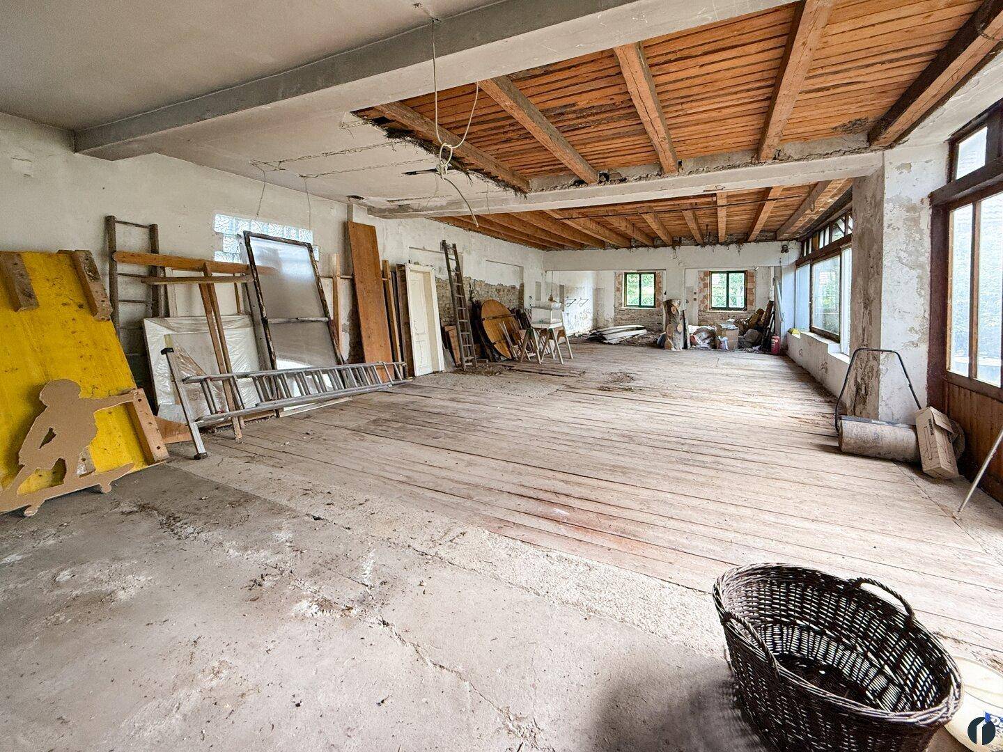 Großer Raum im Rohbau mit sichtbaren Holzbalken und Renovierungsbedarf.