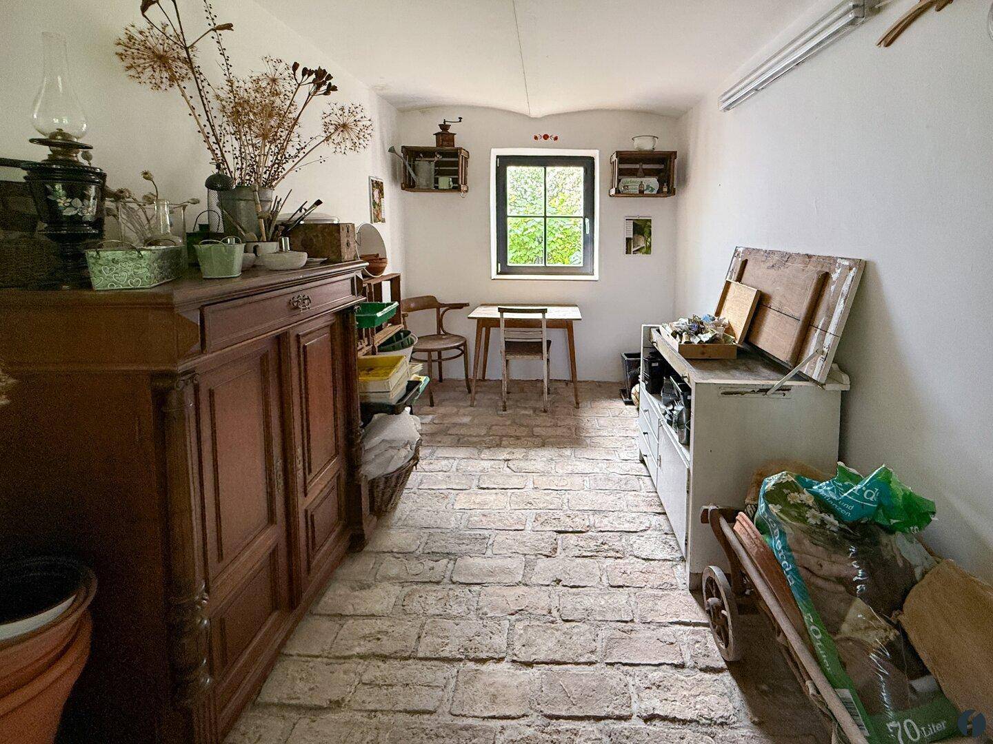 Abstellraum mit Ziegelboden, kleinem Fenster und verschiedenen Möbeln.
