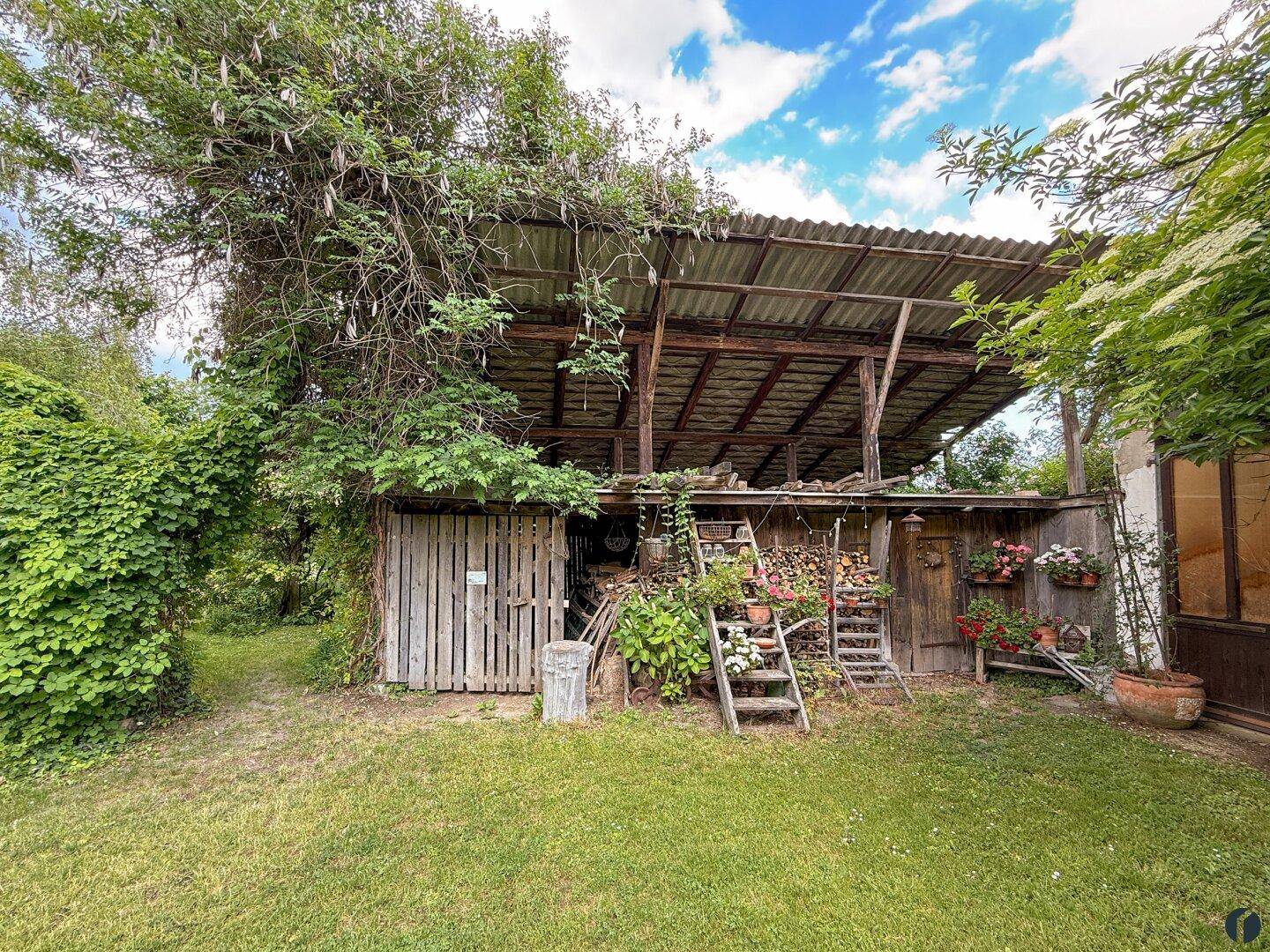 Rustikaler Holzschuppen im Garten, umgeben von üppiger Vegetation.