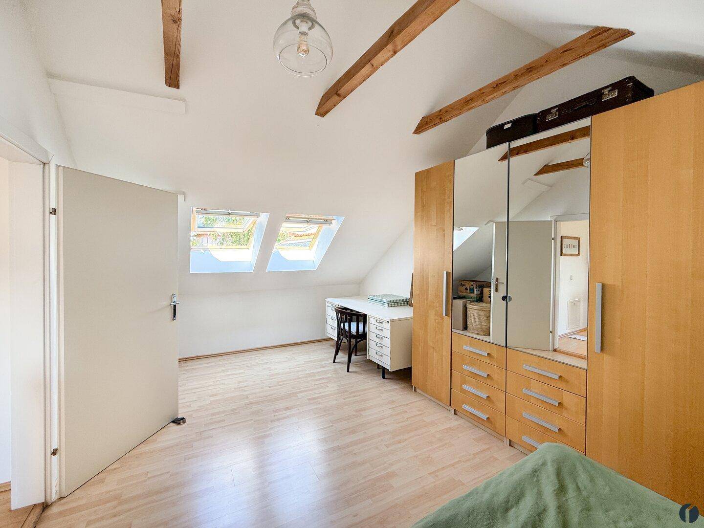 Schlafzimmer im Dachgeschoss mit Dachfenstern, sichtbaren Holzbalken und Kleiderschrank.