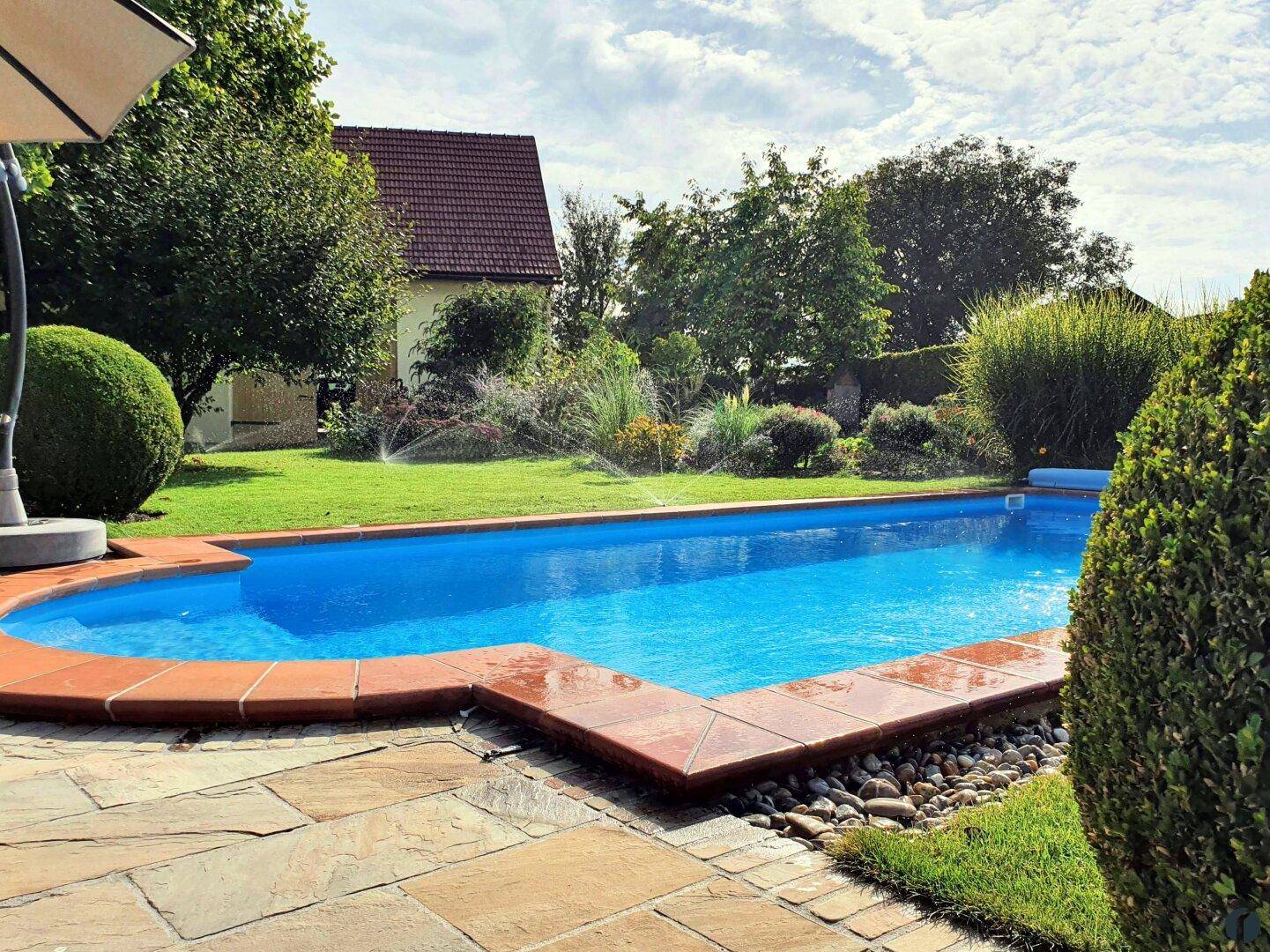 Entspannender Poolbereich im Garten mit Natursteinpflaster und grüner Umgebung.