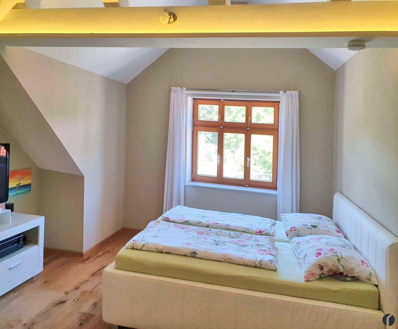 Gemütliches Schlafzimmer im Dachgeschoss mit Holzbalken, Schrägdach und Doppelbett.