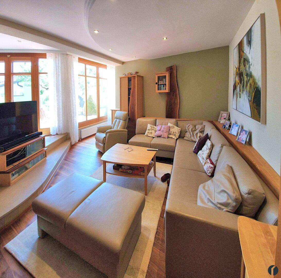 Gemütliches Wohnzimmer mit großem Sofa, Holzboden und indirekter Deckenbeleuchtung.