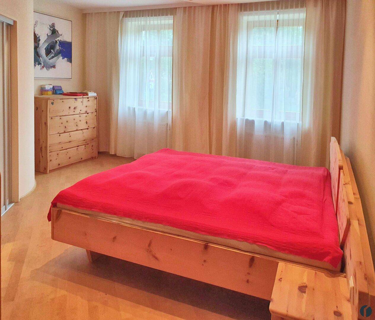 Helles Schlafzimmer mit zwei Fenstern, Holzbett und Kommode, ideal für Ruhe.