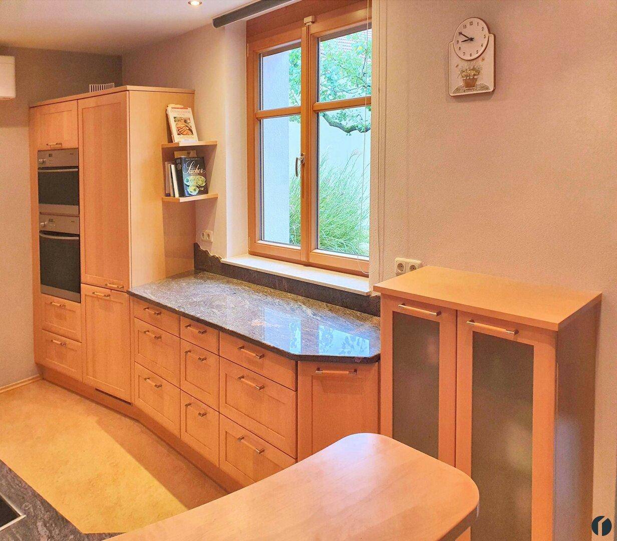 Helle Küche mit Holzfensterrahmen, Granitarbeitsplatte und integrierten Holzschränken.