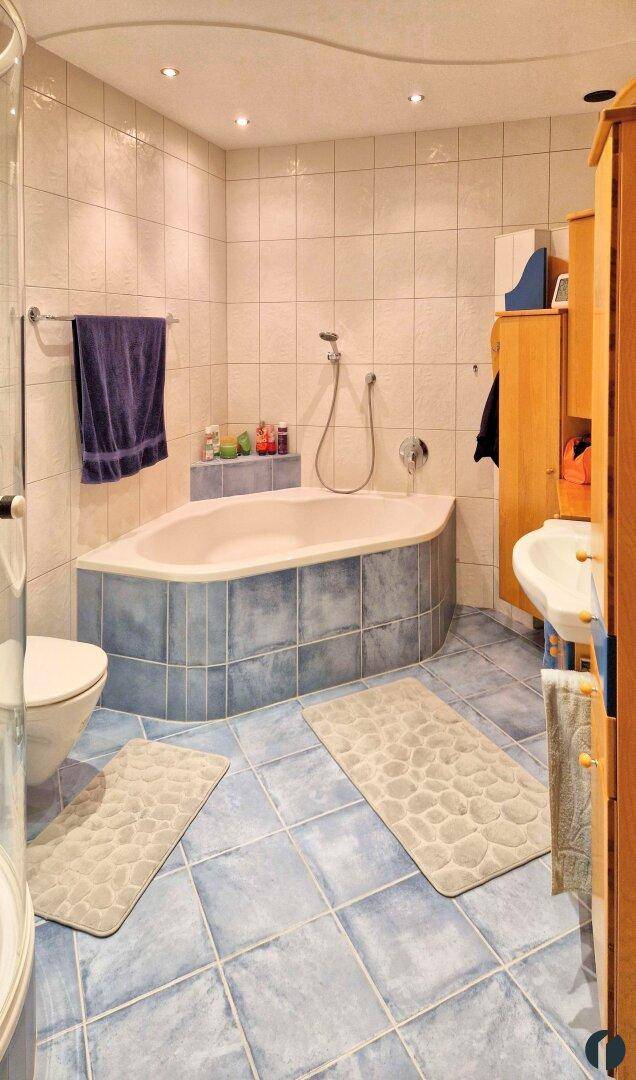 Badezimmer mit blauen Bodenfliesen, Eckbadewanne und wandhängendem WC.
