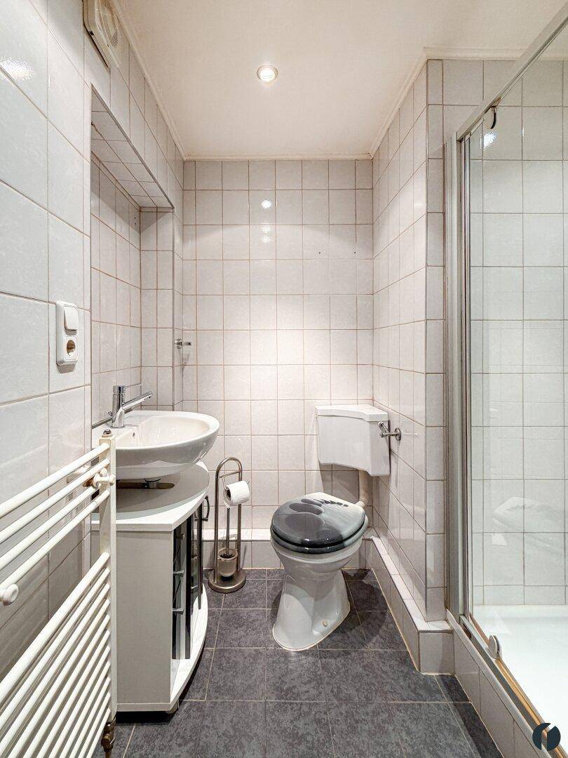 Modern gefliestes Badezimmer mit Waschbecken, Toilette, Dusche und Handtuchheizkörper.
