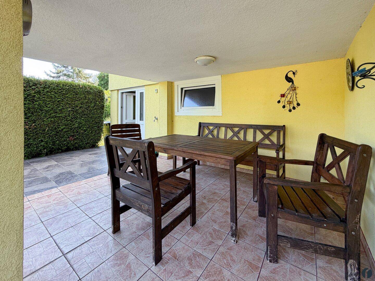 Überdachte Terrasse mit Holztisch und Stühlen, ideal für Mahlzeiten im Freien.