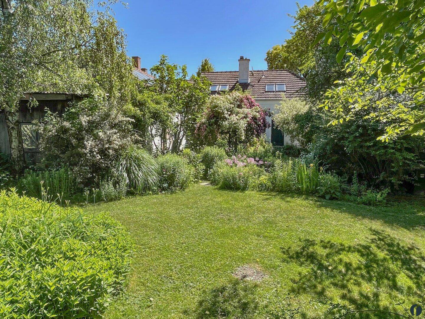 Üppiger Garten mit Rasenfläche und vielfältiger Bepflanzung hinter dem Haus unter blauem Himmel.