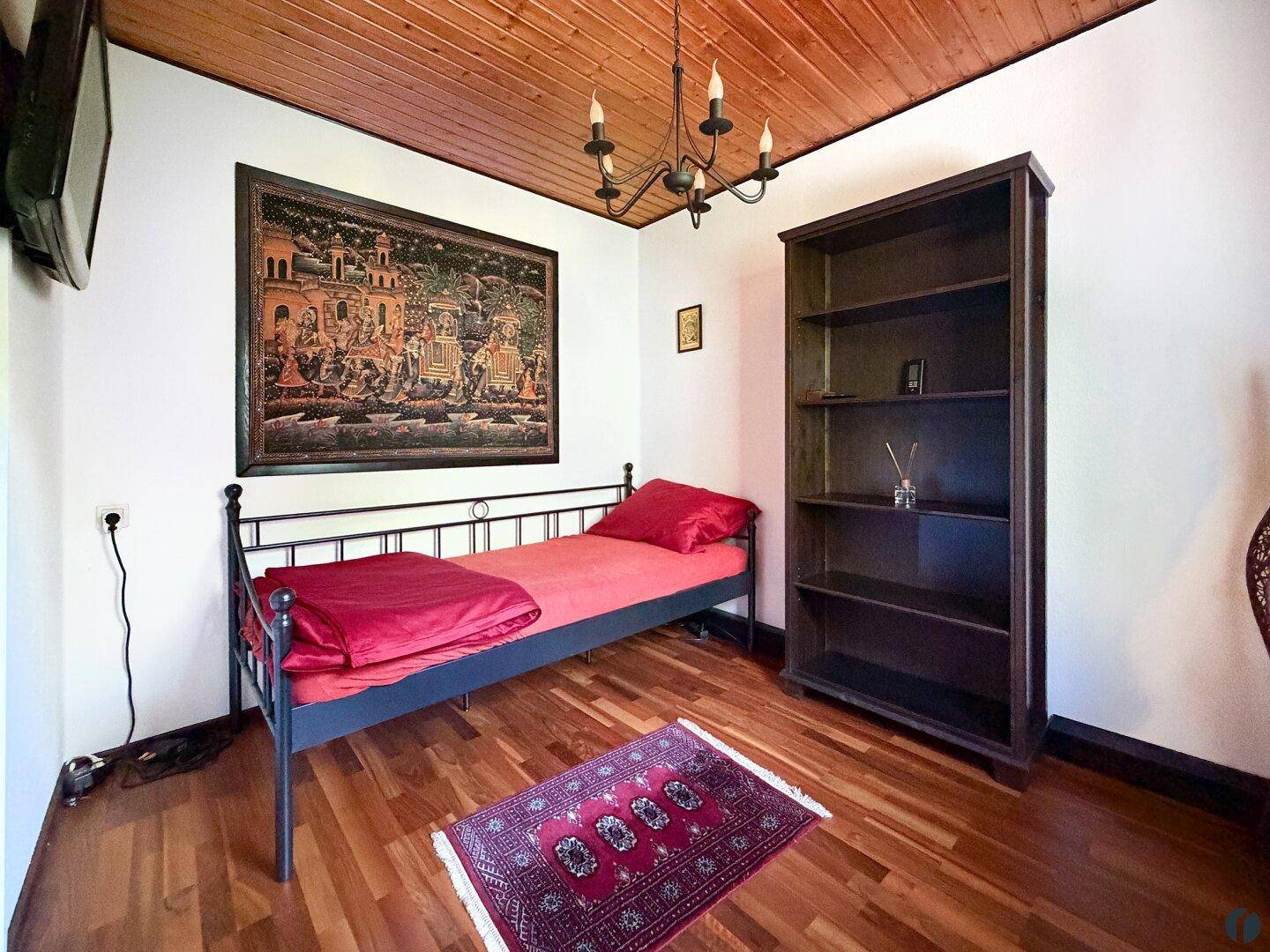 Gemütliches Schlafzimmer mit Einzelbett, Bücherregal und traditioneller Holzdecke.