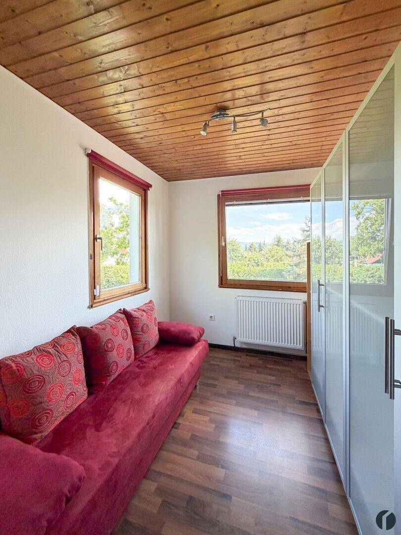 Helles Schlafzimmer mit rotem Schlafsofa, weißem Kleiderschrank und Blick ins Grüne.