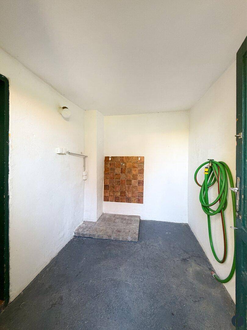Einfacher Hauswirtschaftsraum mit Fliesenbereich und Gartenschlauch, bereit zur Nutzung.