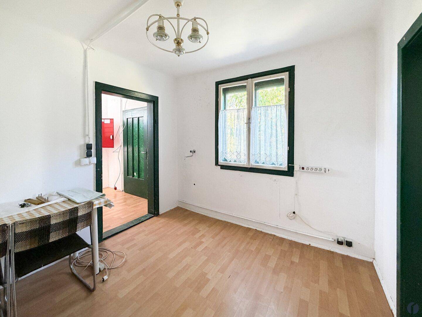 Esszimmer mit Laminatboden, Fenster und einer einfachen Deckenleuchte, bereit zur Renovierung.