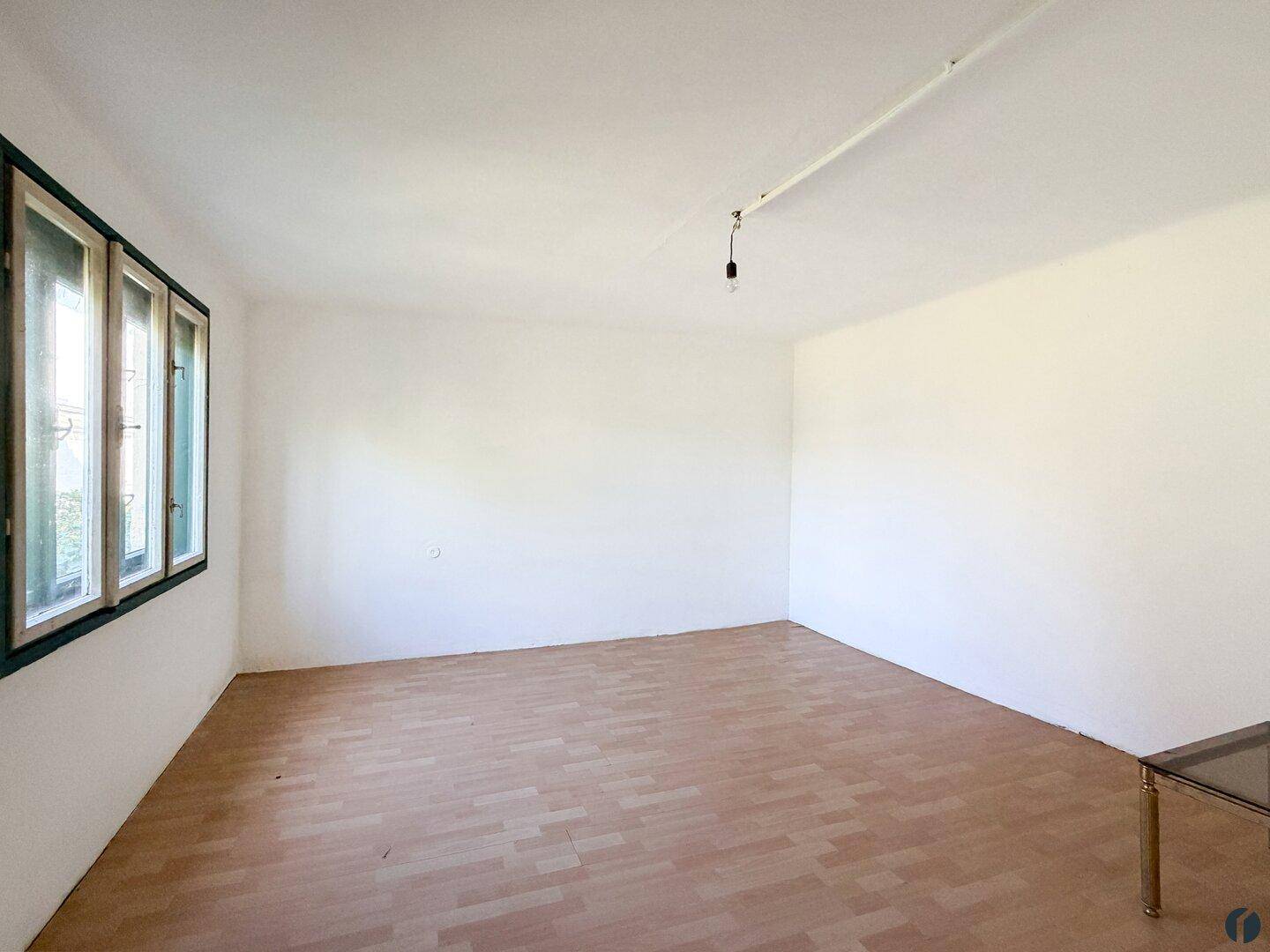 Leeres Wohnzimmer mit Laminatboden und großen Fenstern, die eine Renovierung erwarten.