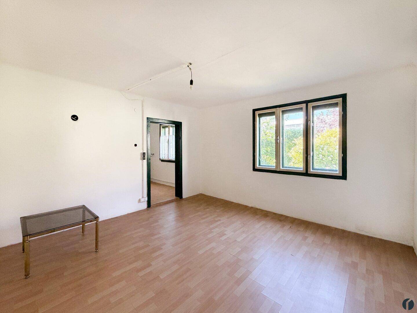 Helles Wohnzimmer mit Laminatboden und großen Fenstern, die viel Tageslicht hereinlassen.