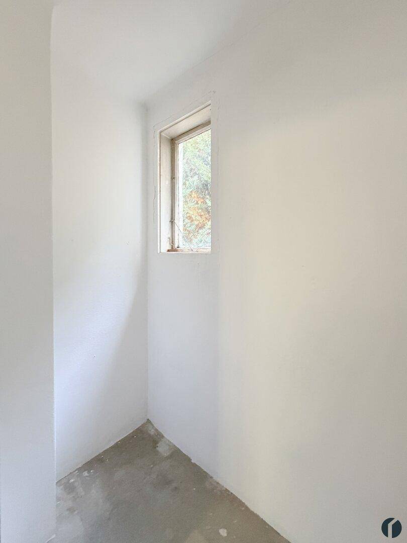 Kleiner, heller Abstellraum mit einem Fenster und einfachem Betonboden.