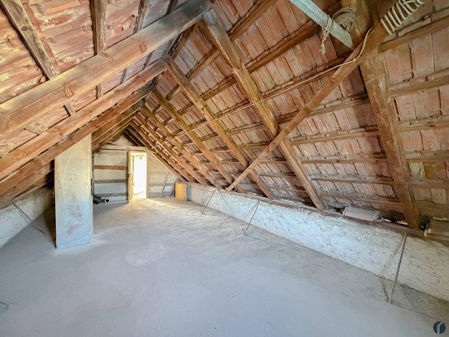 Unausgebauter Dachboden mit Holzdachstuhl und Blick auf einen weiteren Raum.