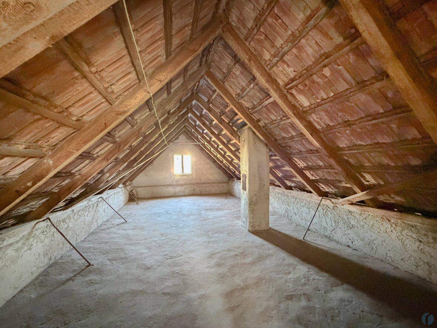 Geräumiger Dachboden mit sichtbaren Holzbalken und einem kleinen Fenster, ideal für Ausbau.