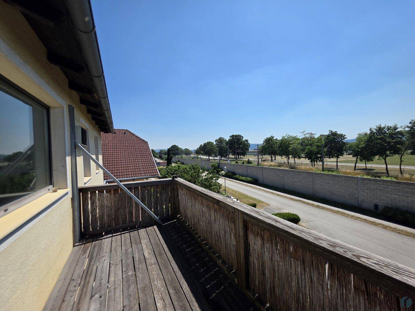 Hölzerner Balkon mit Blick auf die Straße und grüne Bäume unter klarem Himmel.