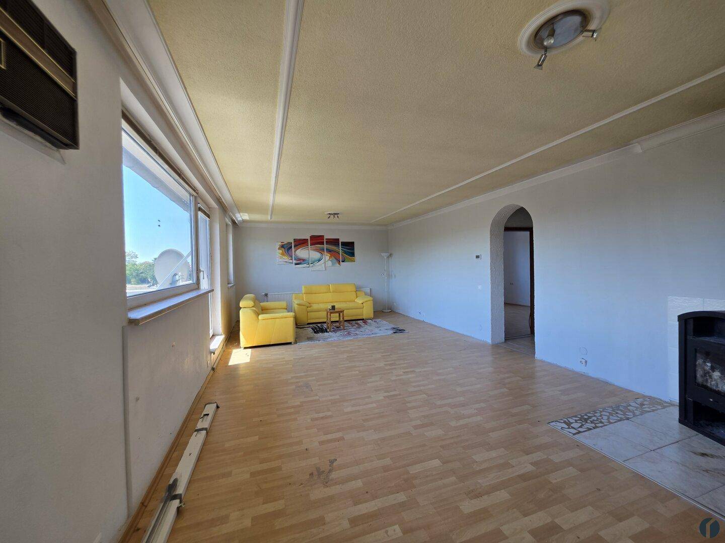 Geräumiges Wohnzimmer mit Parkettboden, großen Fenstern und einem Kaminofen.