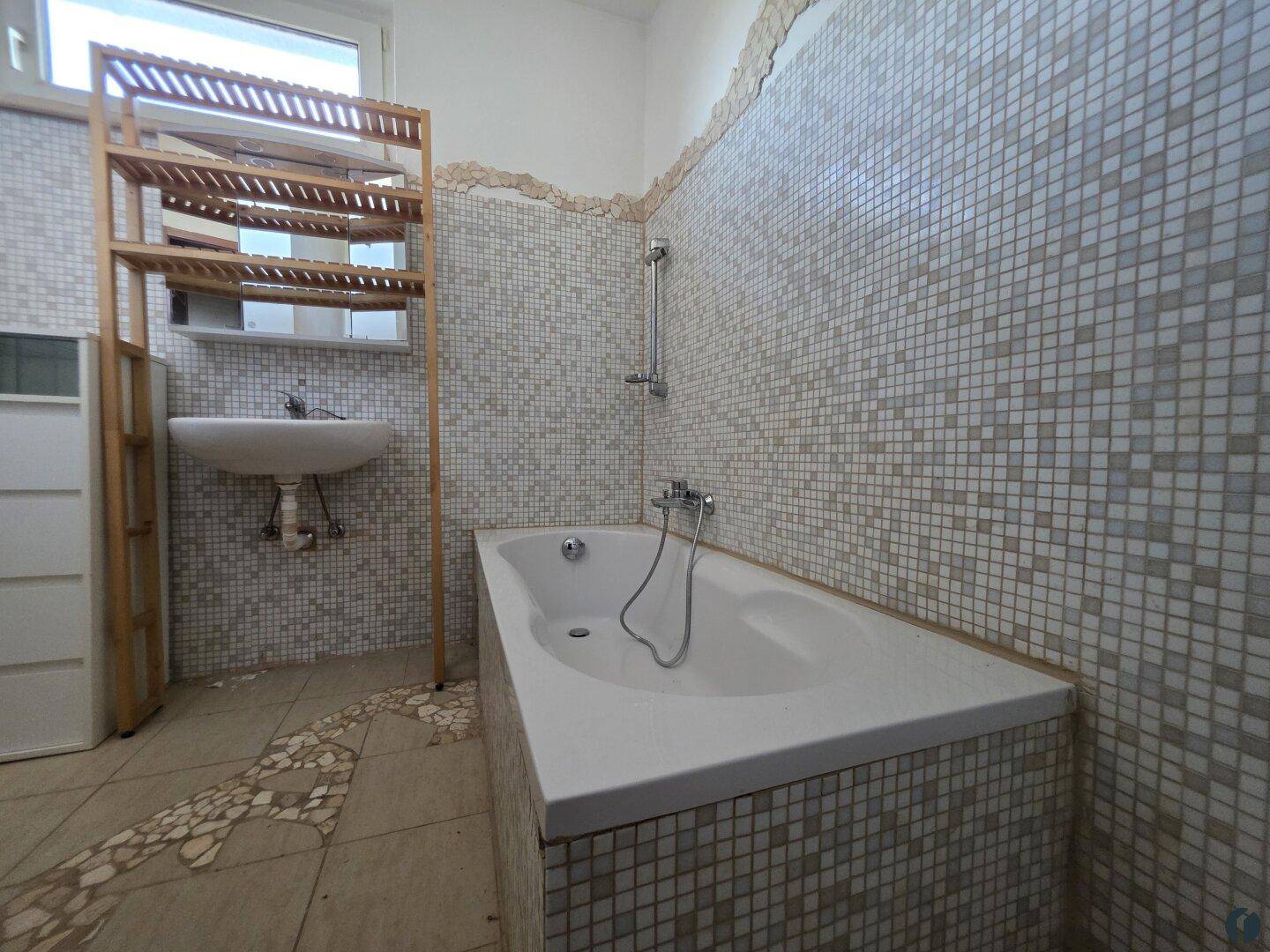 Badezimmer mit Badewanne, Waschbecken und hellen Mosaikfliesen an den Wänden.