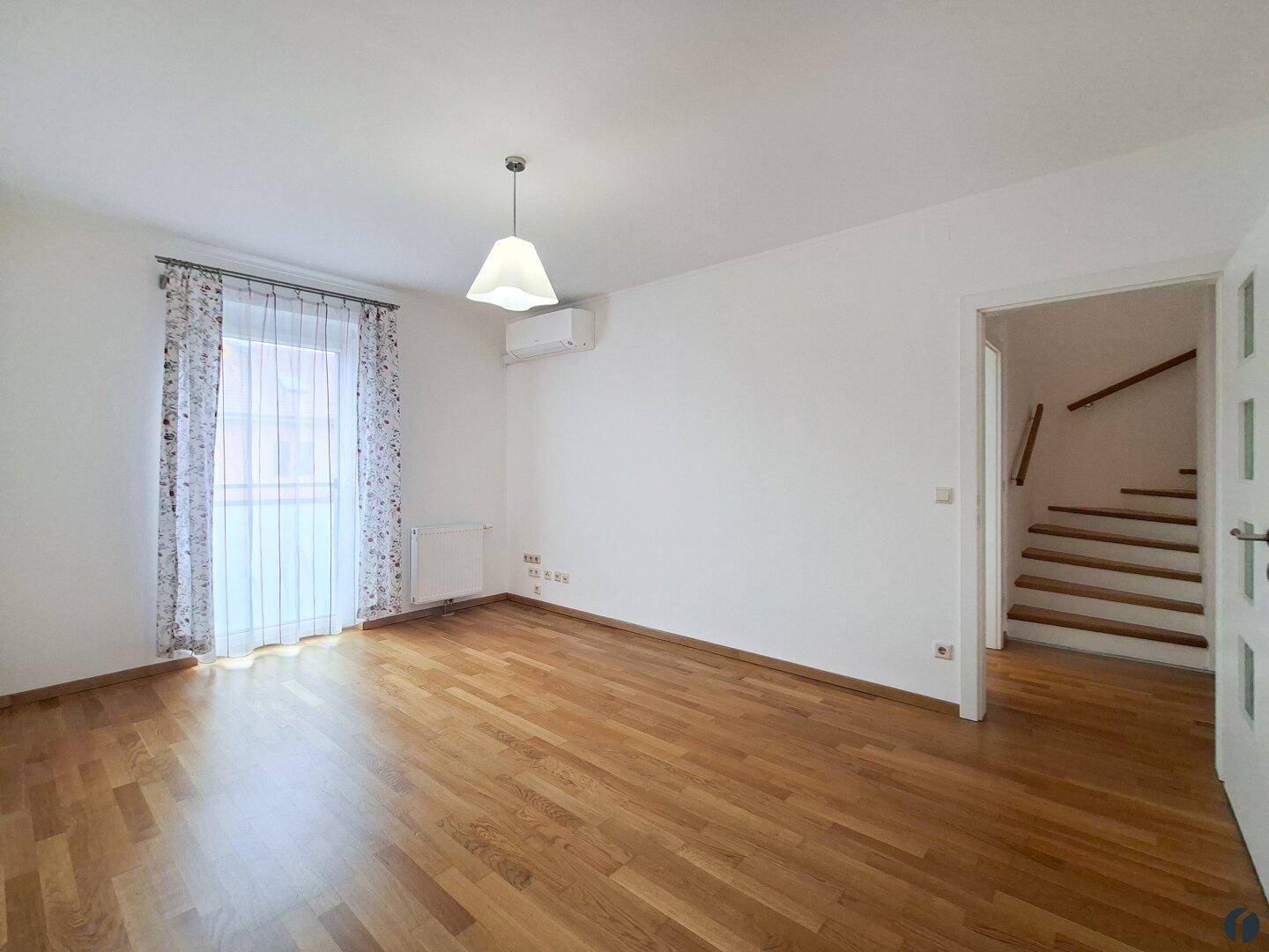 Helles Wohnzimmer mit Holzparkettboden, Klimaanlage und Treppenaufgang.