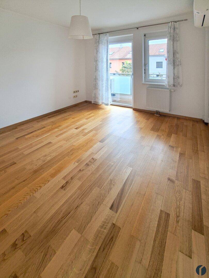 Helles Zimmer mit Holzparkettboden und Zugang zu einem Balkon.