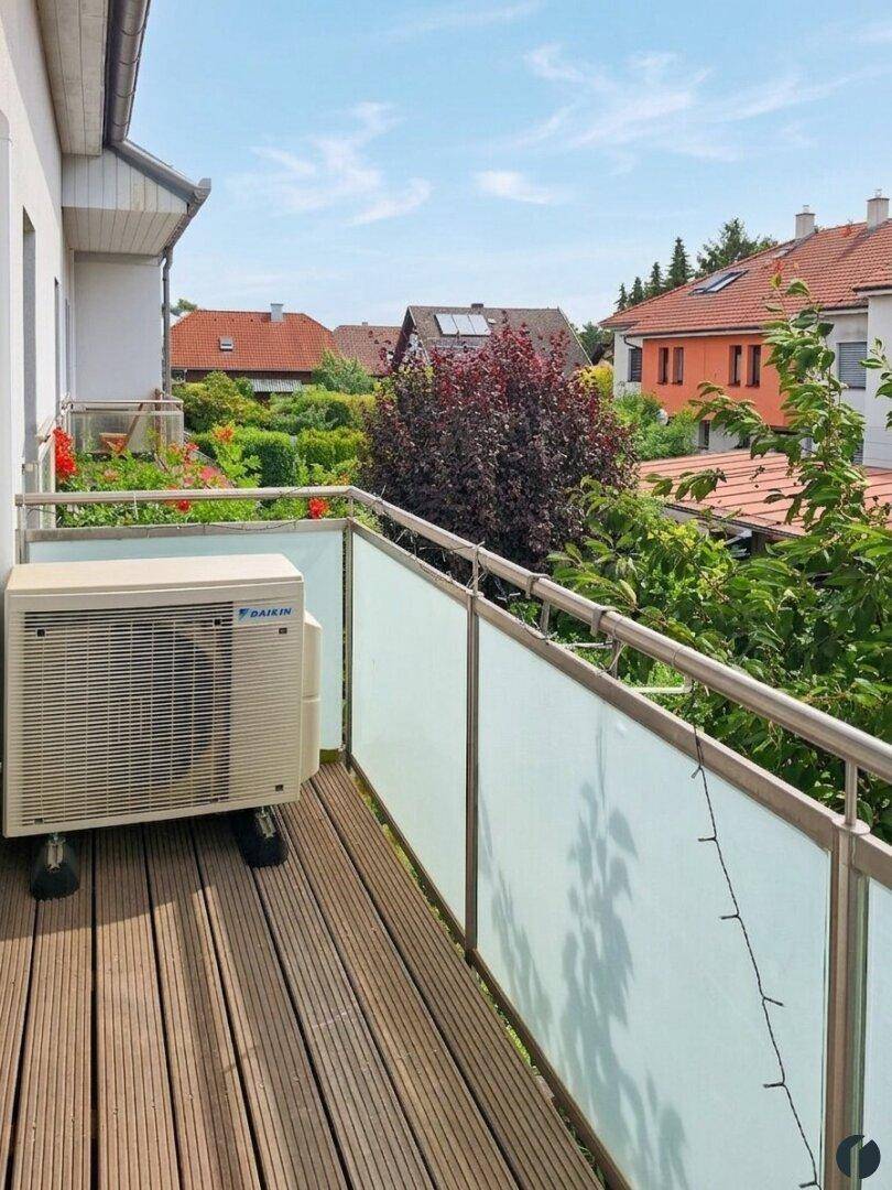 Balkon mit Holzboden, Glasbrüstung und Klimaanlage-Außengerät.