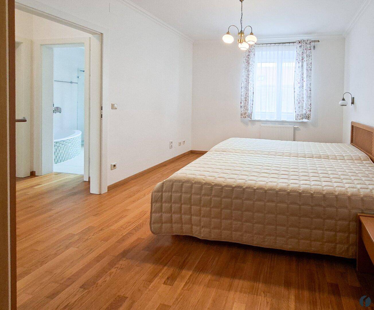 Schlafzimmer mit Doppelbett, Holzparkettboden und Zugang zum Badezimmer.