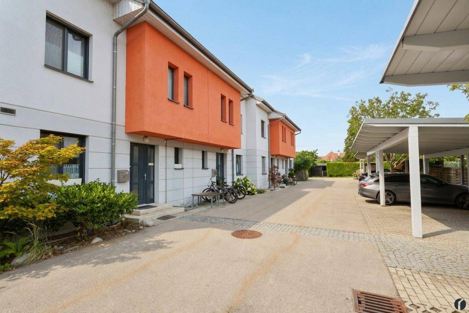 Moderne Reihenhäuser mit orangefarbenen Akzenten und Carport-Parkplätzen.