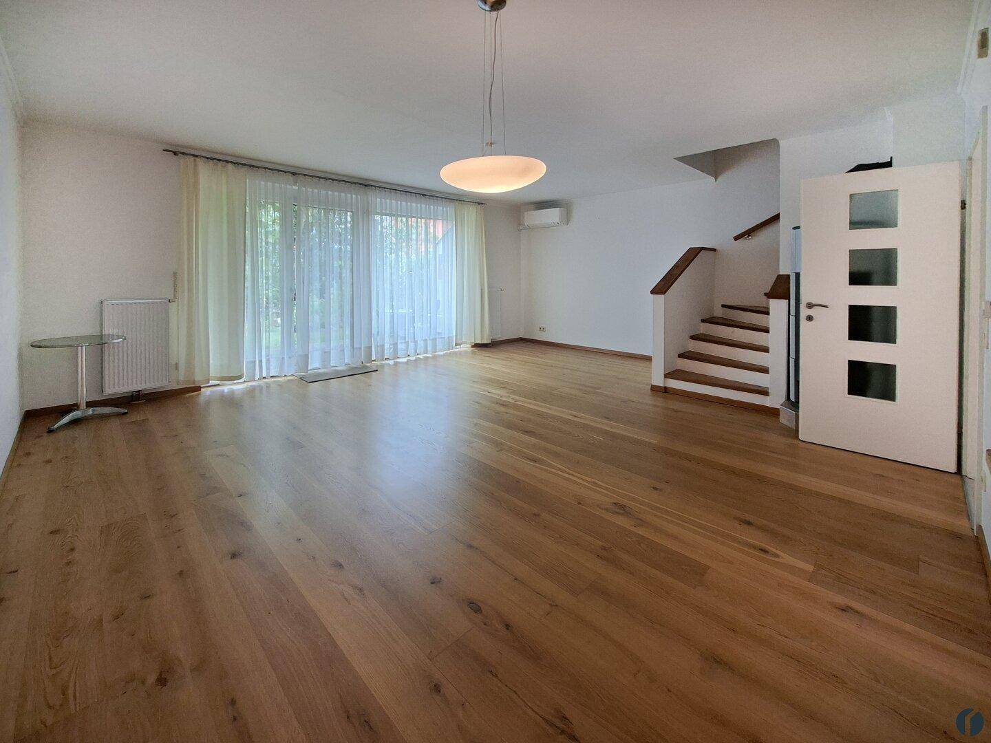 Helles, leeres Wohnzimmer mit Holzparkettboden und Treppenaufgang.