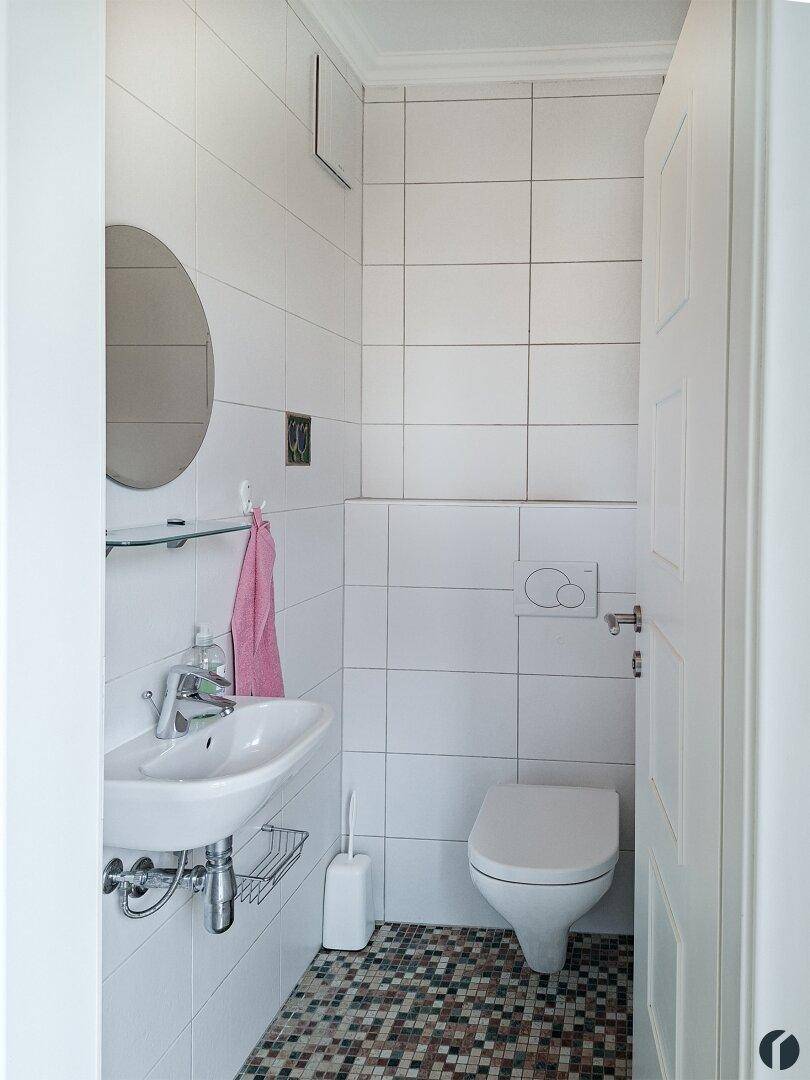 Kleines Gäste-WC mit weißen Fliesen und Mosaikboden.