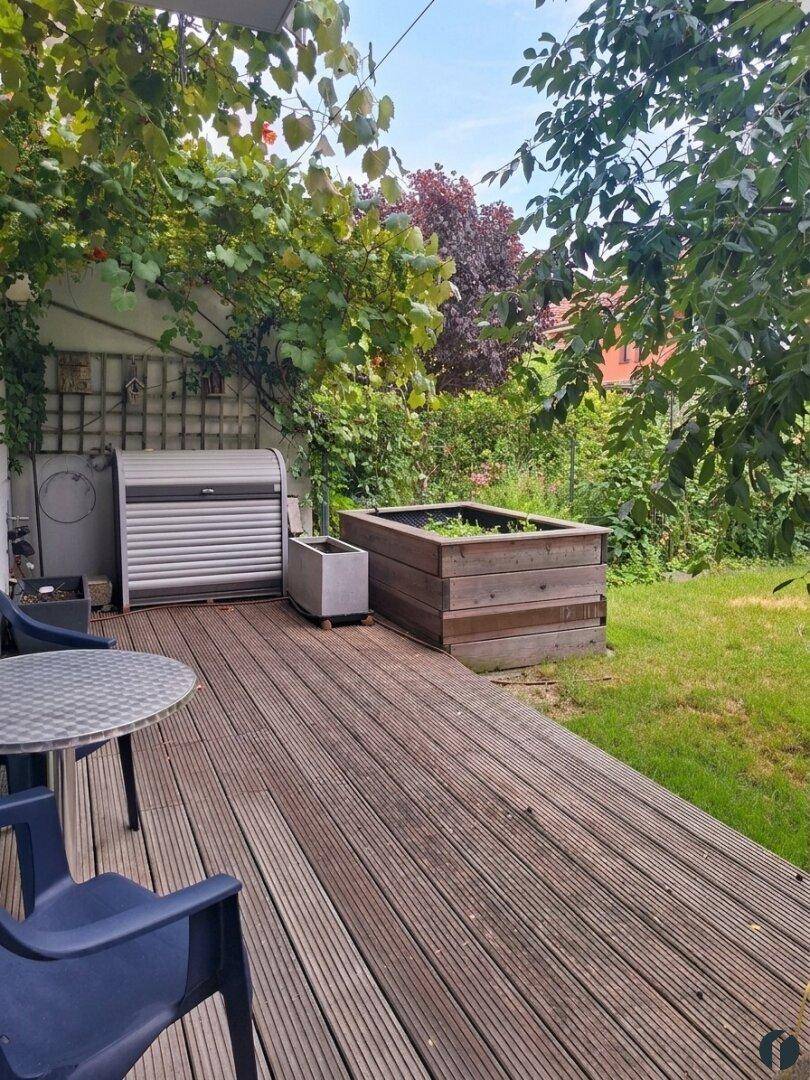 Holzterrasse mit Hochbeet und Sitzgelegenheit im grünen Außenbereich.