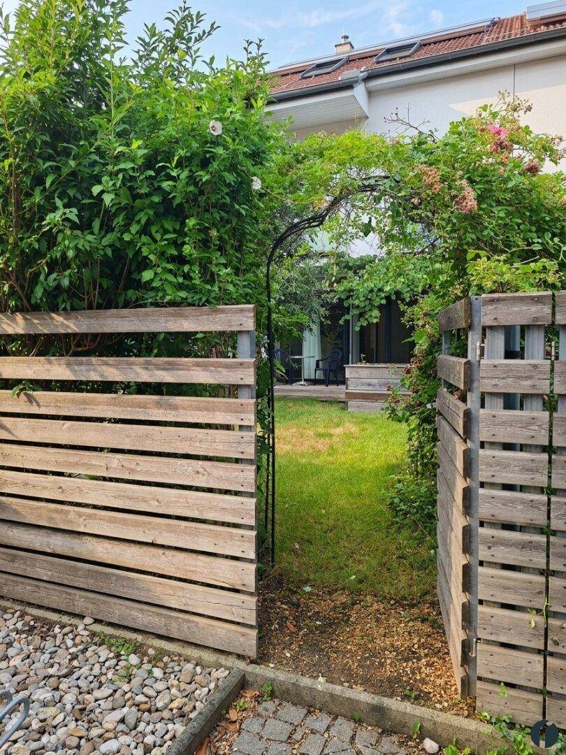 Holzzaun und Gartentor führen zu einem grünen Gartenbereich.