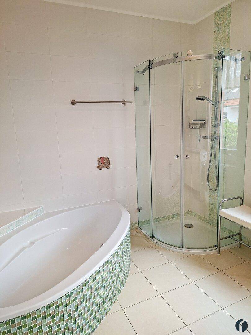 Badezimmer mit Badewanne, Duschkabine und hellen Fliesen.