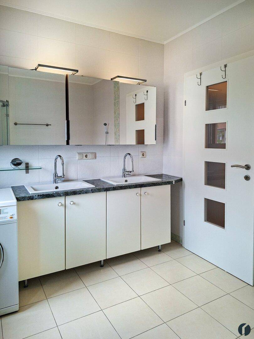 Badezimmer mit Doppelwaschbecken, Spiegelschrank und Waschmaschine.