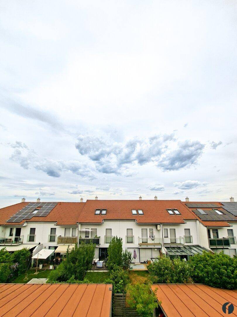 Reihenhäuser mit roten Ziegeldächern und Solaranlagen unter bewölktem Himmel.