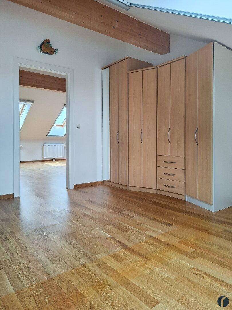 Schlafzimmer mit Holzparkett und Einbauschränken, Blick in einen weiteren Raum mit Dachfenstern.