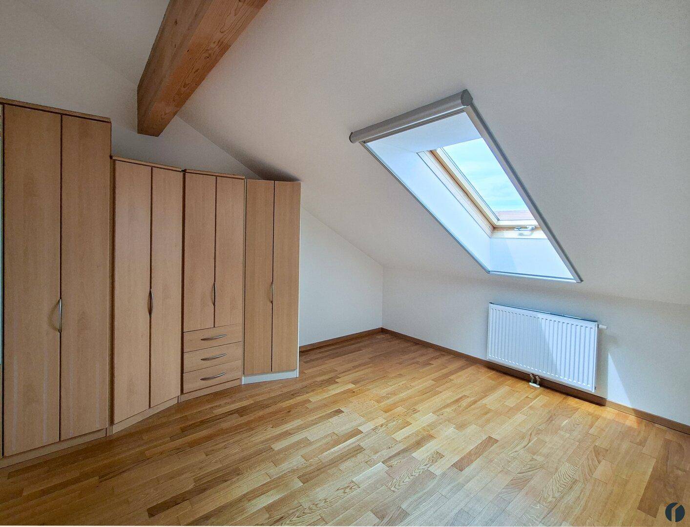 Gemütliches Schlafzimmer im Dachgeschoss mit Einbauschränken, Parkettboden und einem Dachfenster.