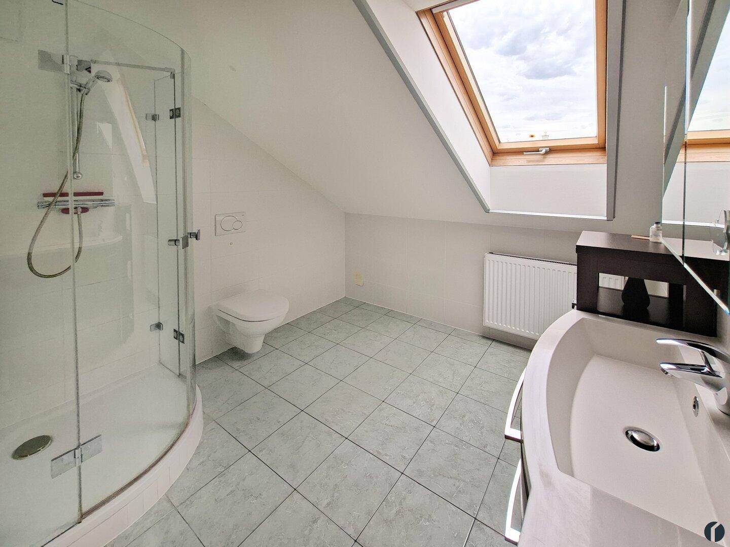 Modernes Badezimmer im Dachgeschoss mit Dusche, WC, Waschbecken und großem Dachfenster.