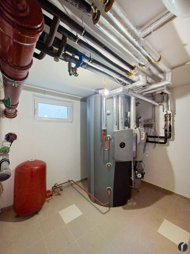 Technikraum im Keller mit Heizungsanlage, Warmwasserspeicher und sichtbaren Rohrleitungen.