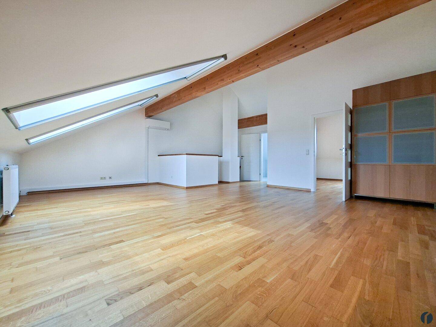 Helles Dachgeschoss-Wohnzimmer mit Holzbalken, Parkettboden und Dachfenstern, bietet viel natürliches Licht.