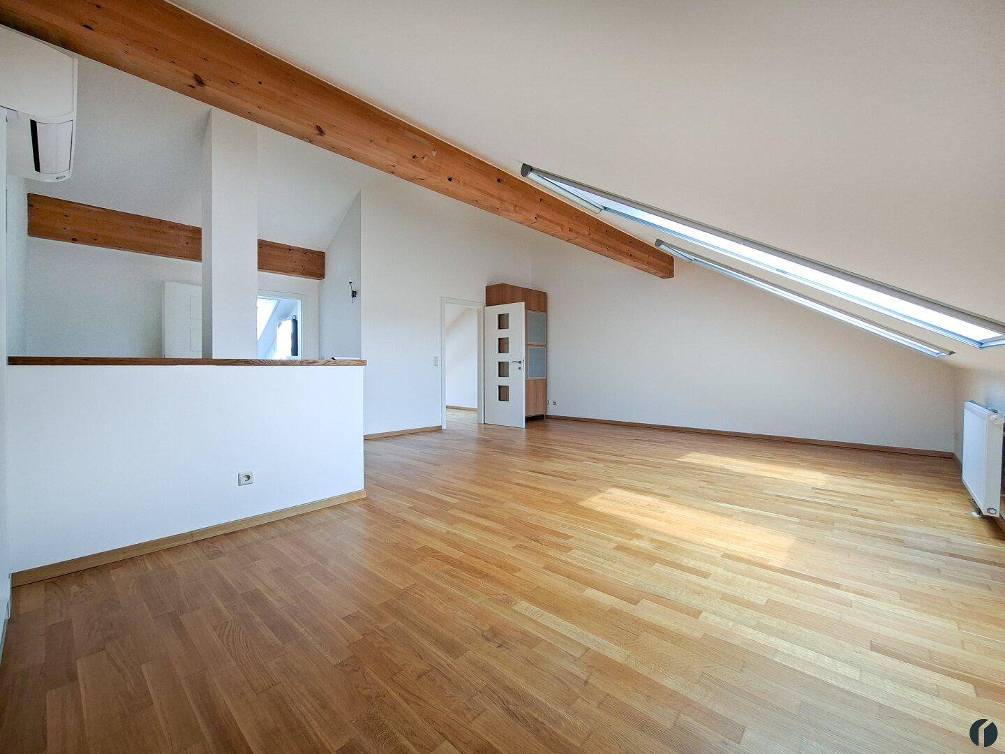 Geräumiges Wohnzimmer im Dachgeschoss mit sichtbaren Holzbalken, schrägen Dachfenstern und Klimaanlage.
