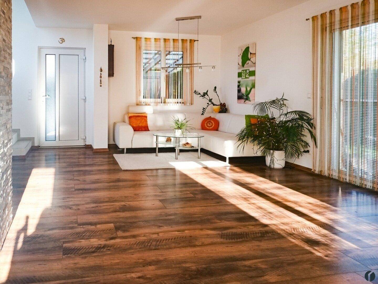 Helles Wohnzimmer mit Holzboden, weißem Ecksofa und Zugang zur Terrasse.