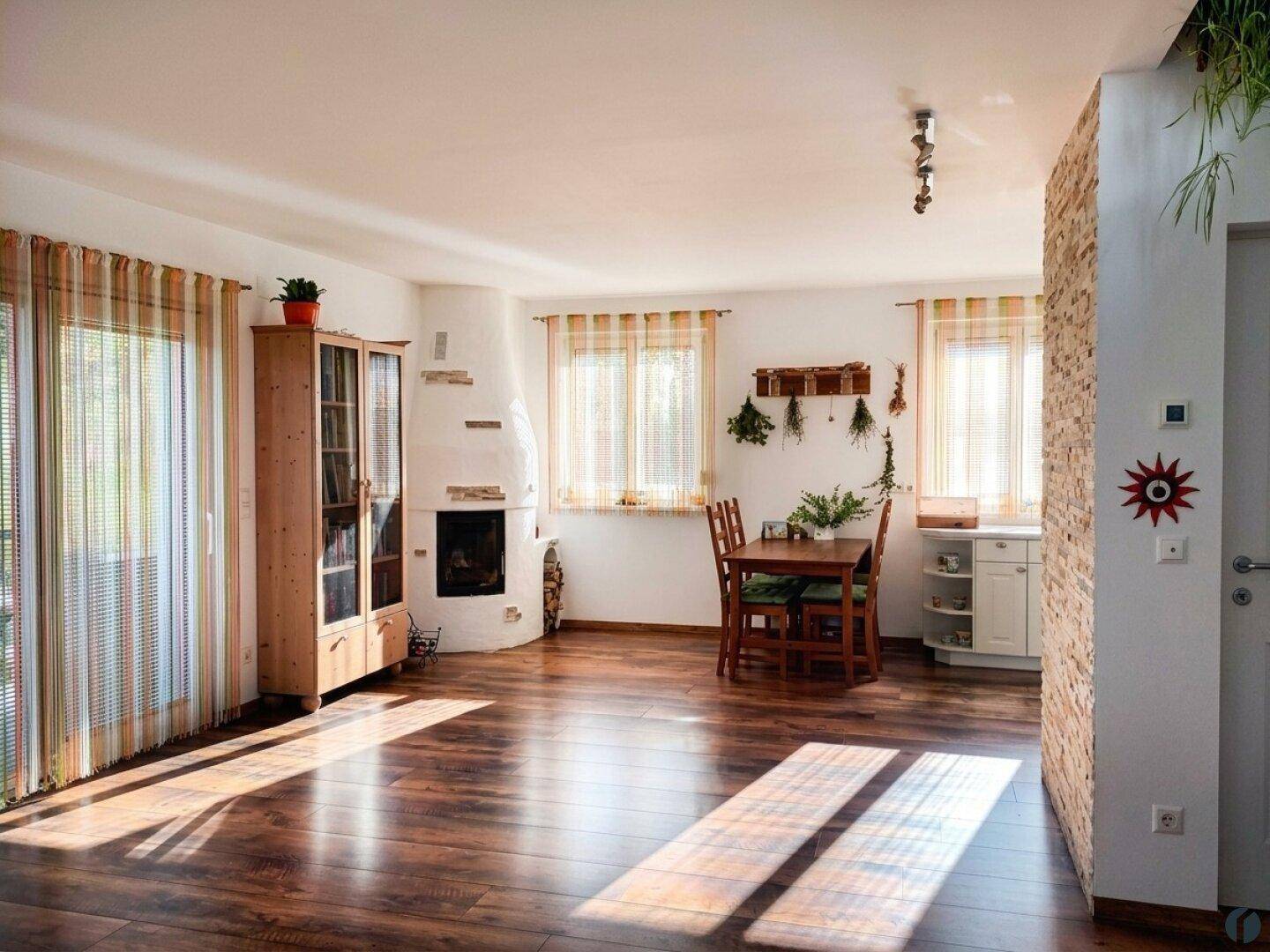 Geräumiger Wohn-Essbereich mit Holzboden, Kamin und Esstisch, durchflutet von Sonnenlicht.