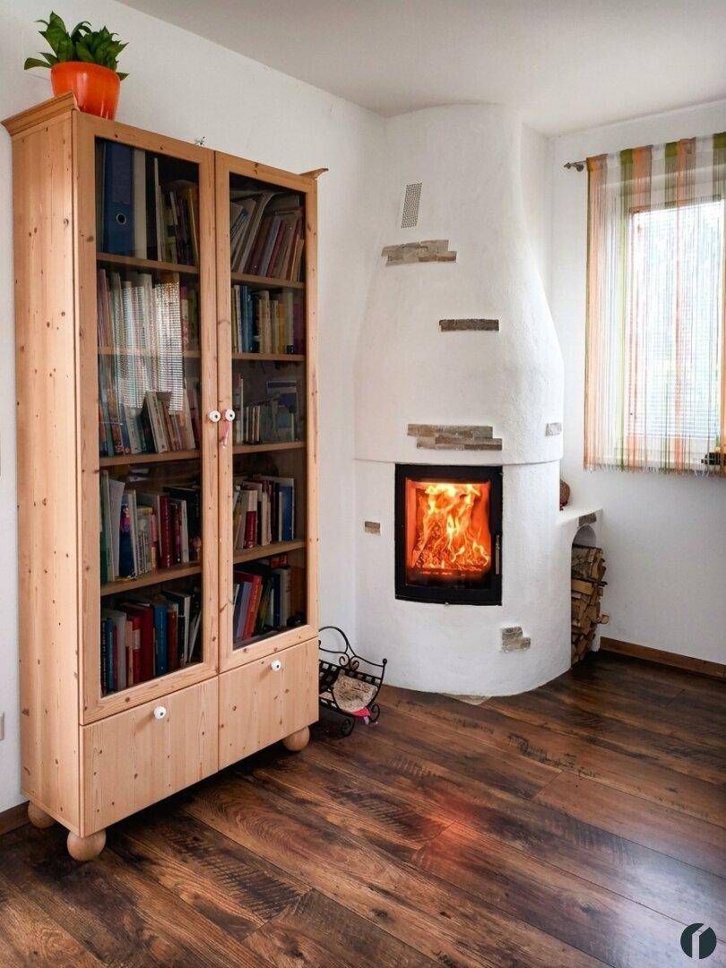 Gemütlicher Kaminbereich mit brennendem Feuer und einem Bücherregal aus hellem Holz.