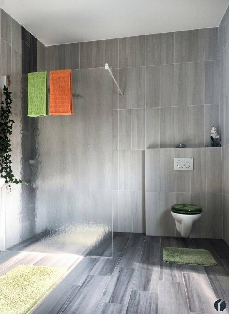 Modernes Badezimmer mit grauen Fliesen, begehbarer Dusche und wandhängendem WC.