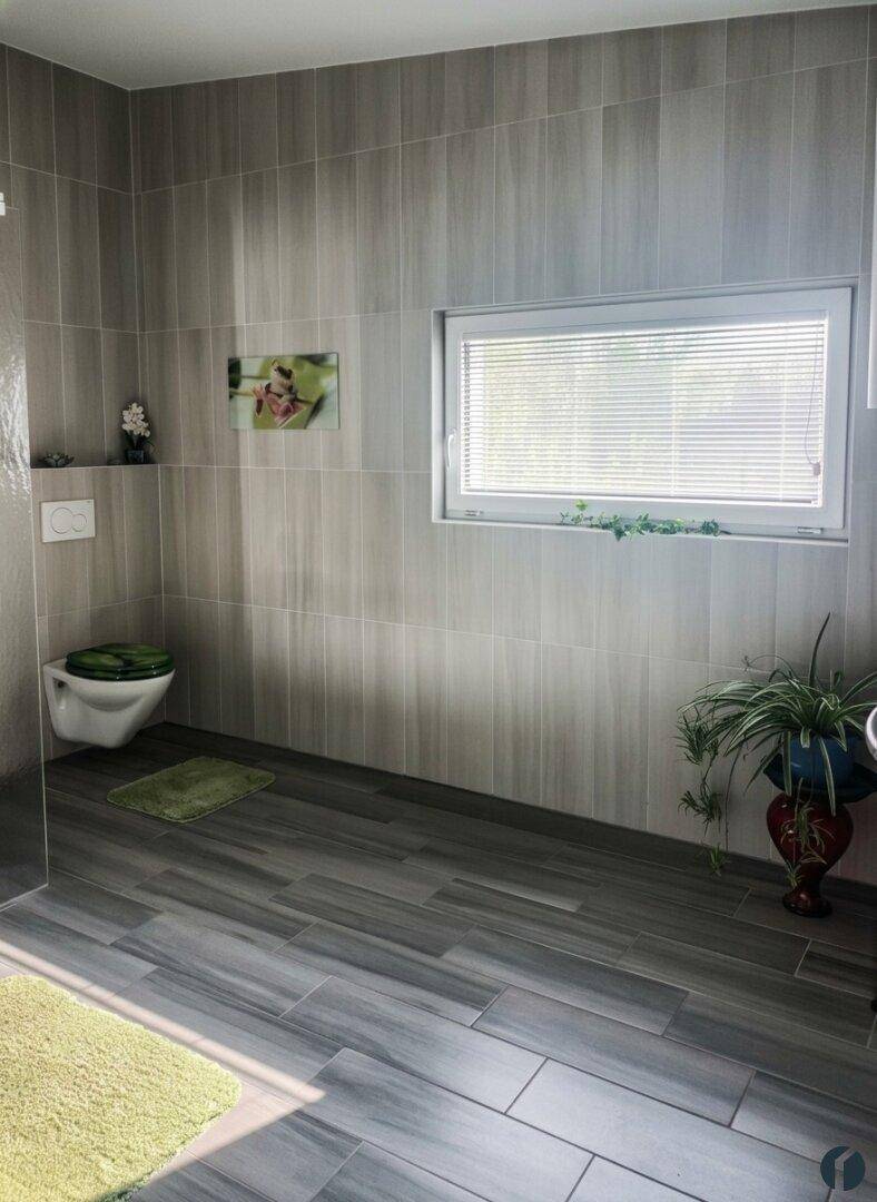 Helles Badezimmer mit grauen Fliesen, Fenster und wandhängendem WC, gut beleuchtet.